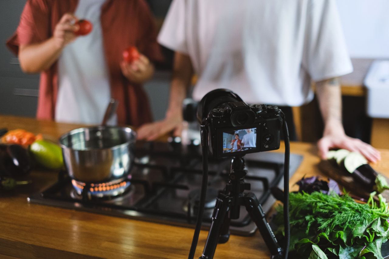 Deux personnes filment une vidéo de cuisine avec des légumes frais et une installation caméra sur trépied.